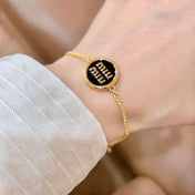 MIUMIU 26S LOGO ROUND BRACELET IN BLACK ENAMEL AND GOLD TONE METAL 631809